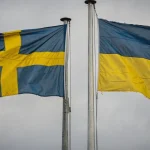 Svenska och ukrainska flaggor sida vid sida mot molnig himmel