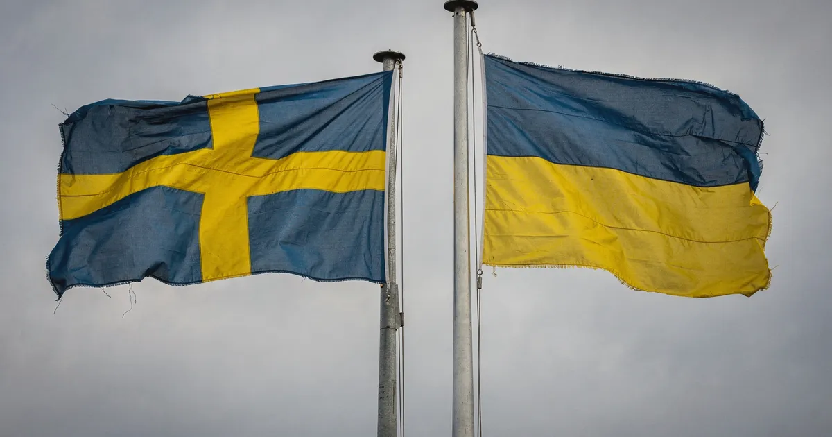 Svenska och ukrainska flaggor sida vid sida mot molnig himmel