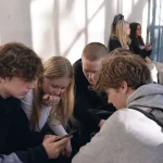 Tonåringar samlade runt en telefon i en skolkorridor, nyfikna på något de tittar på