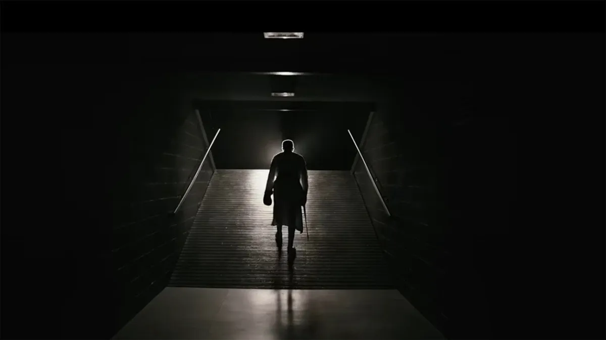 Person i mörk kläder springer genom en lång, mörkläggd tunnel med spotlights uppifrån. Minimalistisk atmosfär med dramaturgi.