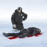 Polis står över liggande person på snötäckt is med blod runt kroppen.