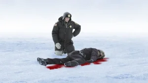Polis står över liggande person på snötäckt is med blod runt kroppen.
